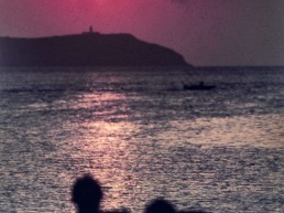 Far de l'illa Sa Conillera mentre uns turistes contemplen la posta de sol.