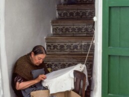 Dona brodant a la porta de casa.