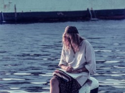 Al port i amb el teló de fons del vaixell de Barcelona una noia descalça, asseguda a un amarrador, es troba absorta en la seva escriptura.